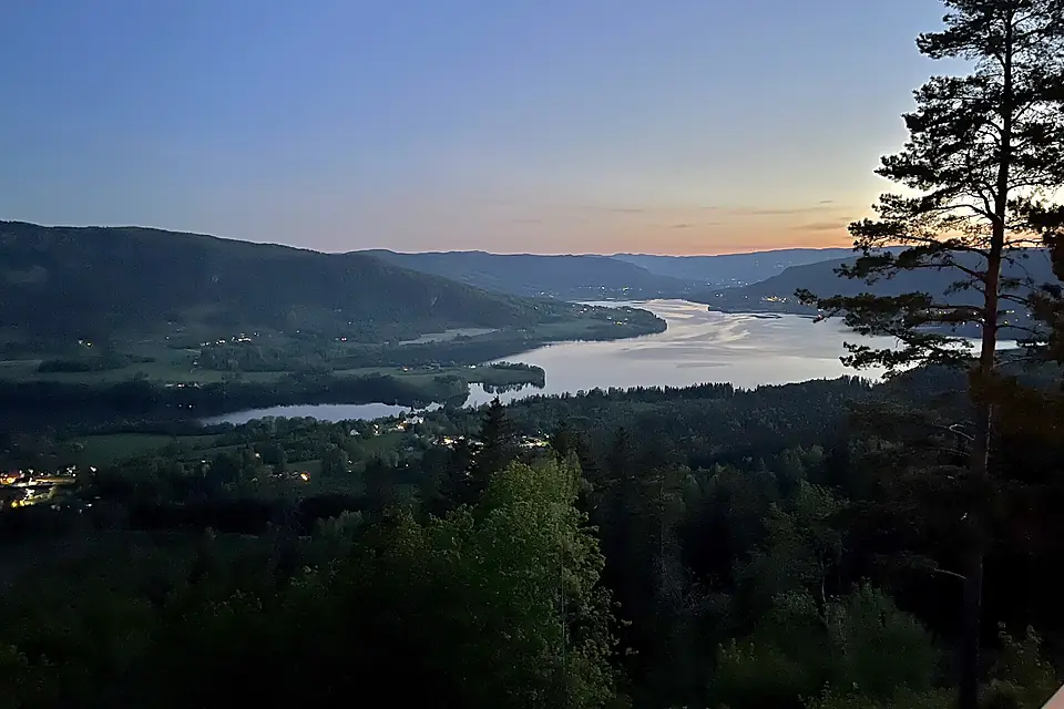 Randsfjorden (nordre ende northern part of lake) Fluberg kirke Odnes Dokkadeltaet, Rostberget etc. Søndre Land municipality Norway. Past midnight sunset glow, forests, hills. View from Granum Gård boarding house 2021-06-01 IMG 1129